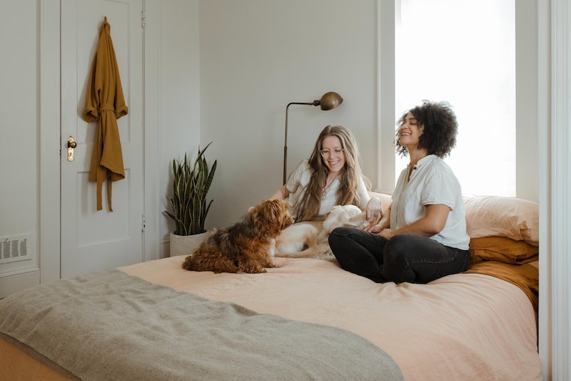 Mujeres sentadas en la cama con su perro en su nuevo departamento propio